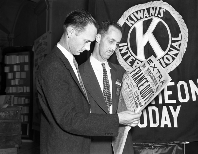 Two men standing and reading the same newspaper