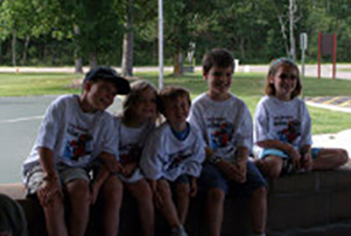 Five kids wearing the same kinds of t-shirts sitting in a park.