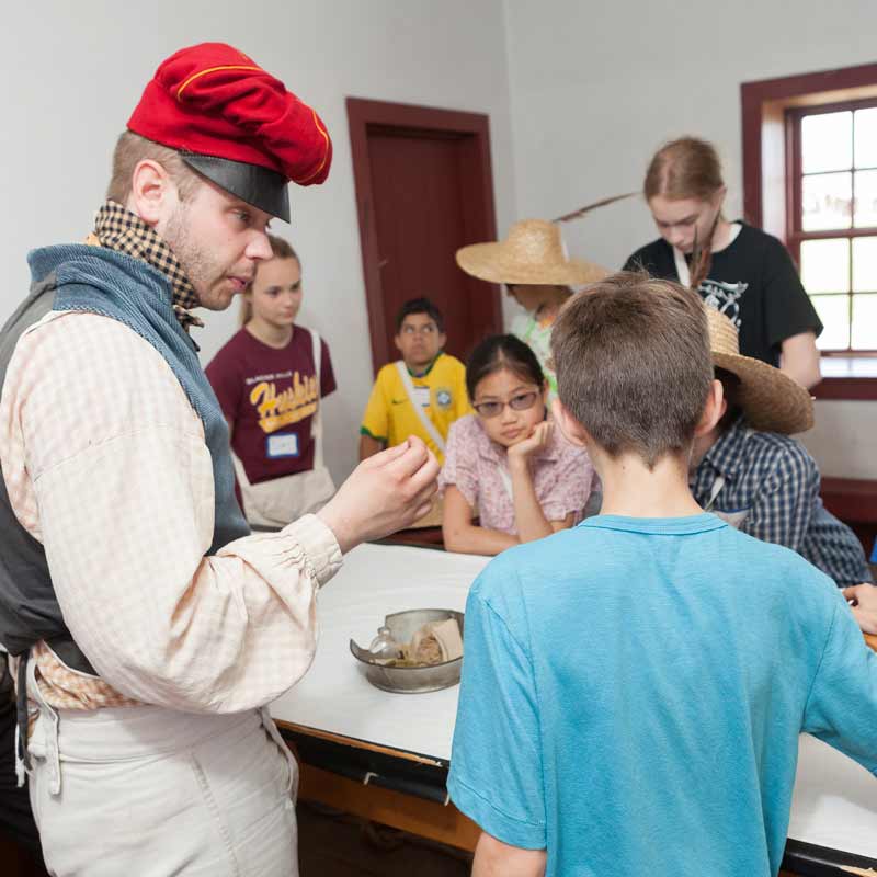 A costumed teacher portraying an engineer at Fort Snelling speaking with enthusiasm to a group of kids.