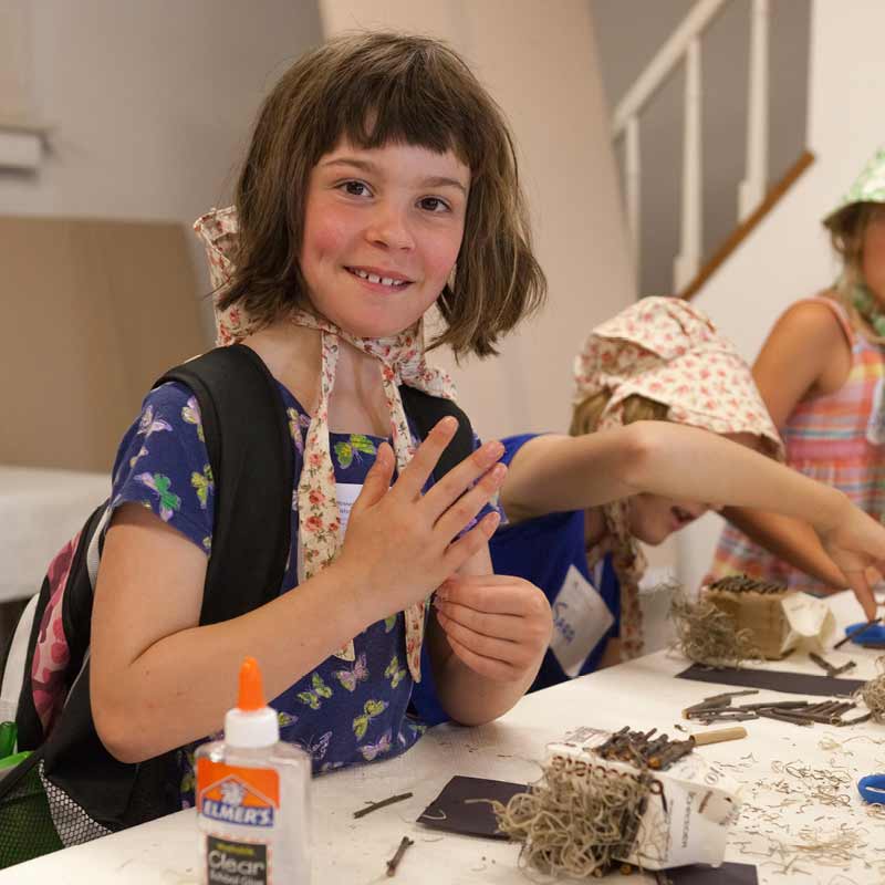 Young girls in bonnets making a craft.