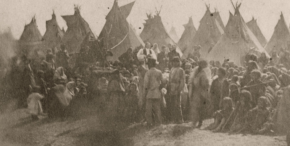 Historic photo of people gather in front of tipis.