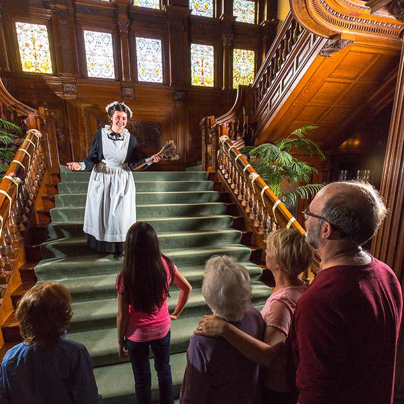 Woman dressed as maid standing on main staircase in front of tour group