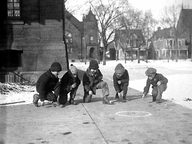 Photo of five young boys playing marbles on the sidewalk, ca. 1925.