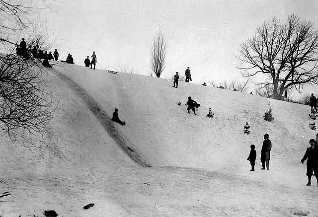 Photo of snowy hill with children sledding.
