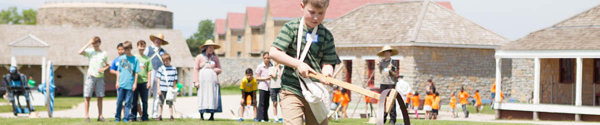 A group of children play historic yard games on the lawn of Fort Snelling.