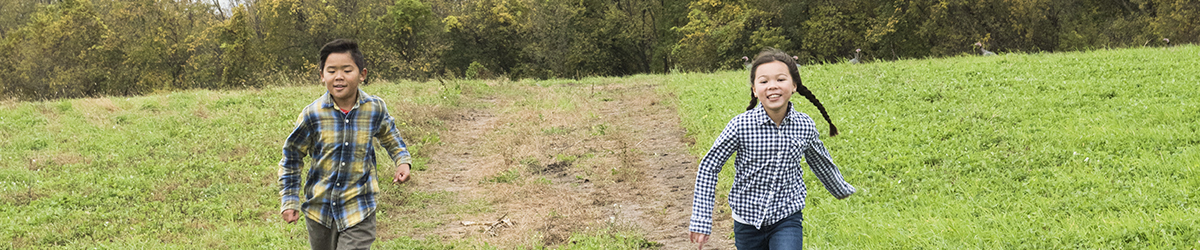 A boy and a girl running on a dirt path toward the camera