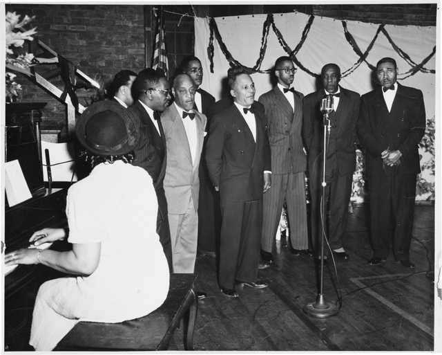 A group of men sing in front of an audience at Phyllis Wheatley Community Center.
