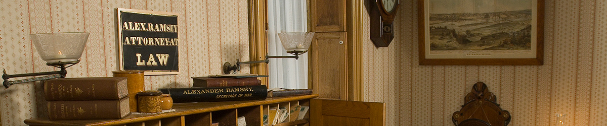 Ramsey's office. Books on desk, plaque that reads Alex. Ramsey Attorney at Law