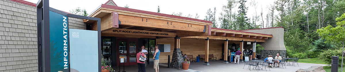 Closeup of an information panel next to a one-story wood building with people in front