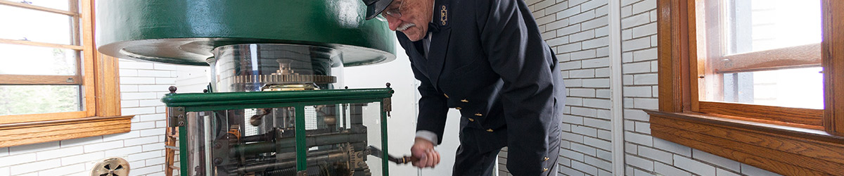 A lighthouse keeper turning a crank to rotate the lens