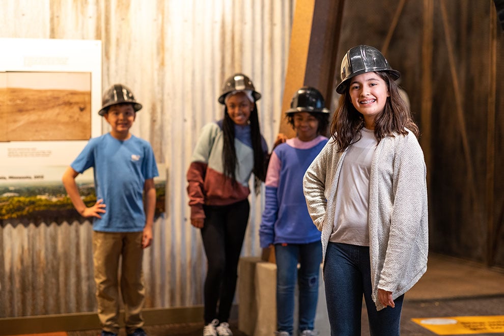 Four students wearing helmets in the history center exhibit.