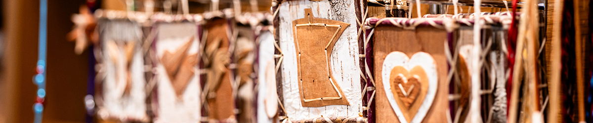 A close-up of hanging, rustic ornaments made from birch bark and stitched string, featuring wooden cutouts including the shape of the state of Minnesota and a layered heart.
