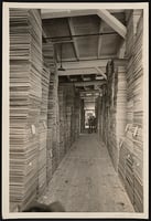 Stacks of milled lumber inside a lumber mill, with stacks piled up on either side of an empty walkway