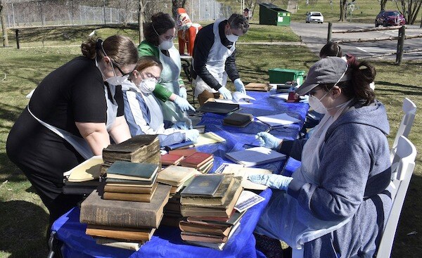 Seven people at two tables set up outside  working with moldy artifacts