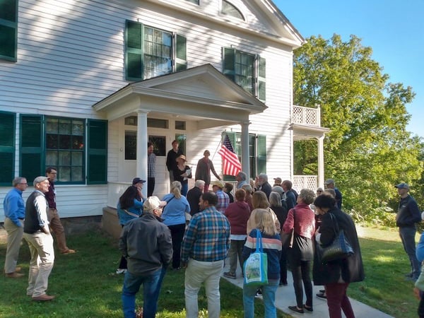 Tour group of 20-30 people standing in front of house museum listening to tour guide standing on front porch