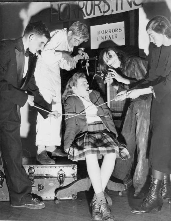 Staged scene of a doctor and his asstant and 2 monsters surrounding tied up teenage girl. ca. 1960s