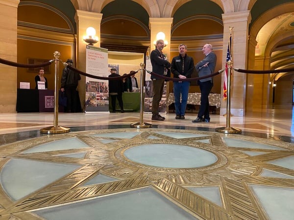 Looking cross North Star in the floor at the MN State Capitol rotunda at three people talking