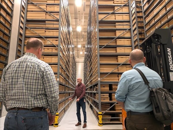 Three people standing and talking in the archive room. Row upon row of boxes are on selving units