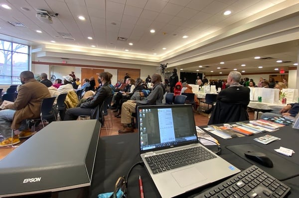 Looking across a table with a scanner set up at people seated watching speakers