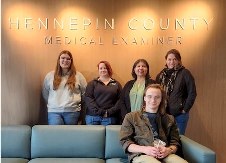 Five staff members standing under a sign Hennepin County Medical Examiner