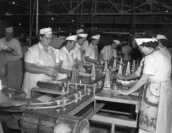 Women on an assembly line processing chicken bits into cans