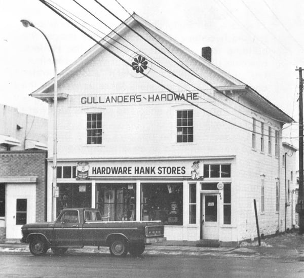 1970s photo of a storefront building - Gullanders Hardware, Hardware Hank Stores. Ford truck is parked in front of it