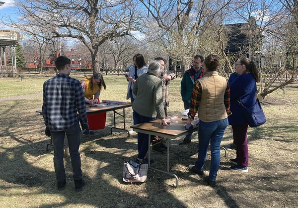 Nine participants in the Finish Workshop outside working on two folding tables at the Ramsey House