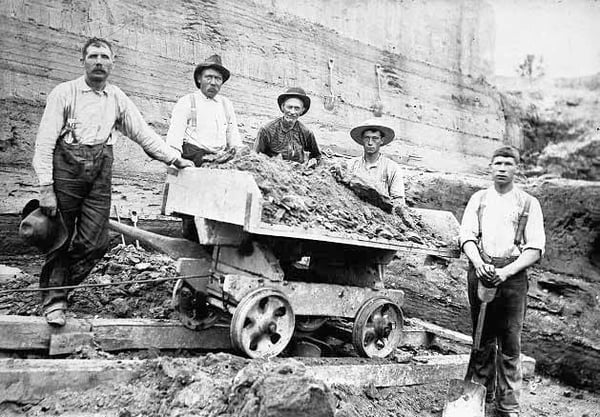 Five workers loading cart in clay pit pose for photo