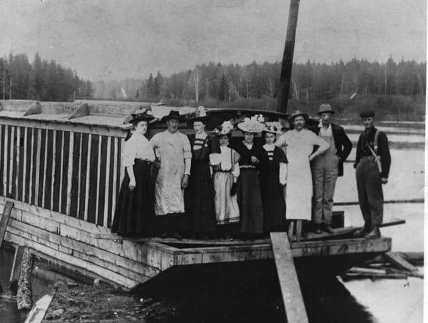Four Men in work clothes and five women in dresses standing on barge on river