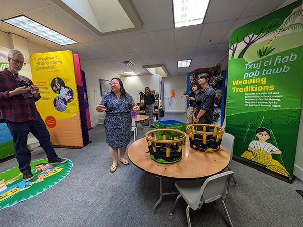  A group of people are engaged with colorful exhibits featuring Hmong weaving traditions and cultural stories inside the Hmong Museum.