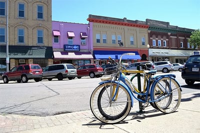 Two bikes parked on the sidewalk, close to the curb, and appear to be securely locked. The commercial main street is lined with various shops and buildings.