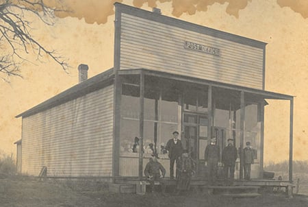 Group of people standing infront of Commercial building with sign saying Post Office. ca. 1900s