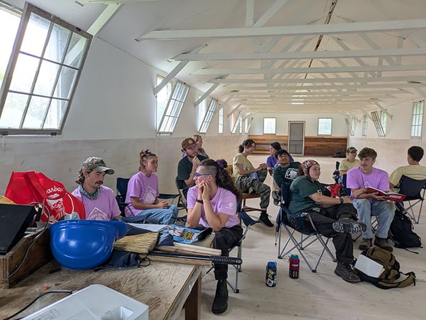 Group of around a dozen young adults sitting and talking to each other in a large white room