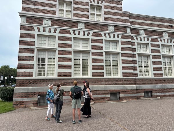 Five people standing outside historic post office building talking to each other and looking at windows