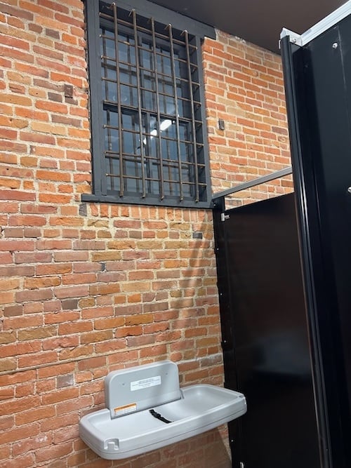Brick wall and barred window with toliet stalls and baby changing station