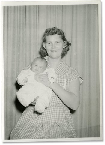 Woman in house dress holding baby-ca.1940s