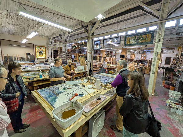 People standing around table in stained glass studio watching demonstration-1