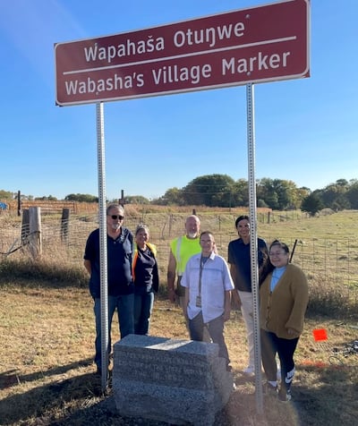 Six people standing behind granite marker. Sign above marker says Wapahasa Otunwe Wabashas Village Marker