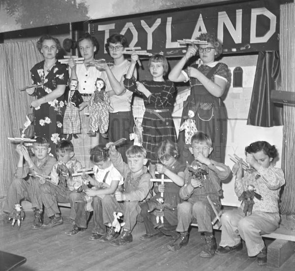 Students and teacher on classroom stage holding marionette puppets