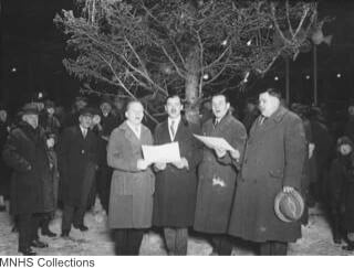 four men caroling outside by christmas tree, 1925