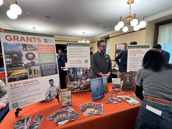 Table with Grants and Local History posters and brochures on it with man standing and talking behind it