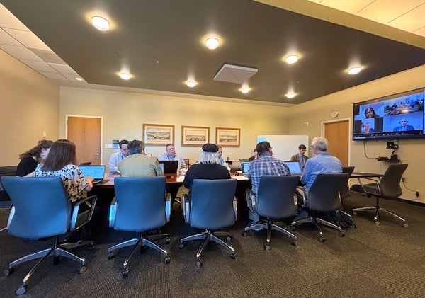 Meeting with people around a conference table, video call on screen