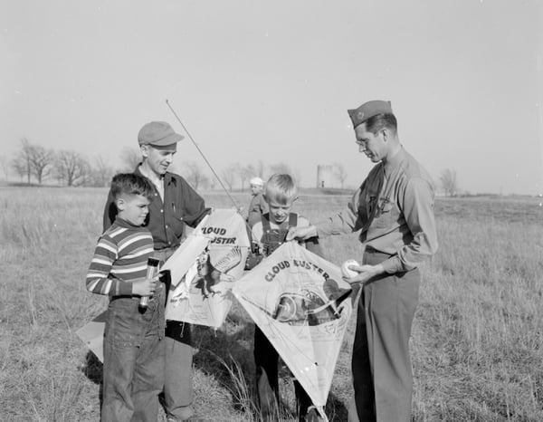 Two boy scouts with a Scout Master and another adult in a field with kites labeled CLOUD BUSTER, About 1950
