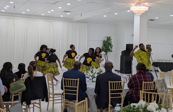 Performers dance on a stage with an audience seated at decorated tables.