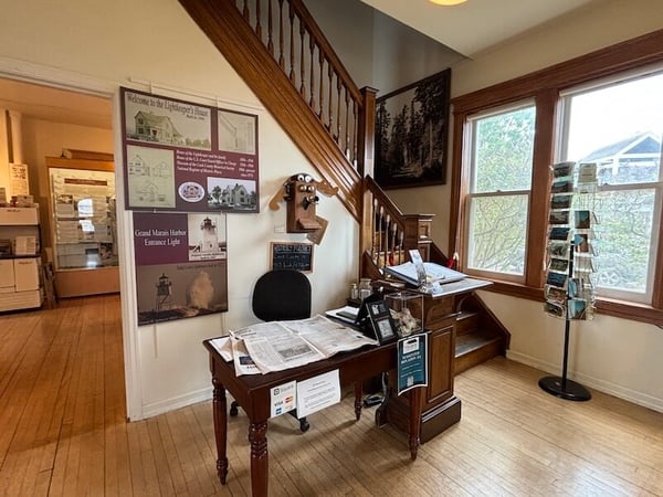 Cook County Museum-Interior of a visitor center with a wooden staircase, desk, posters, and large windows.