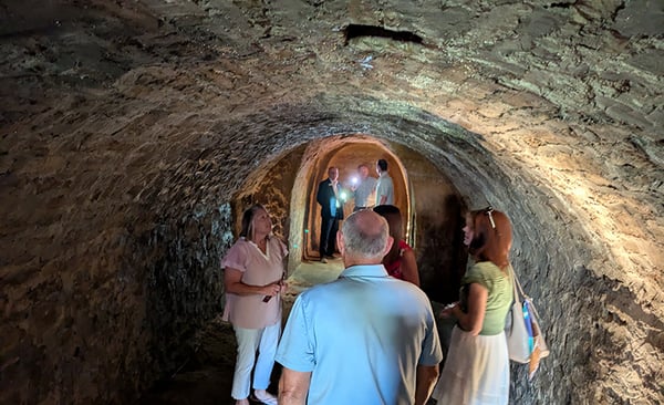 Two groups of people inside a dimly lit underground stone tunnel, engaged in conversation