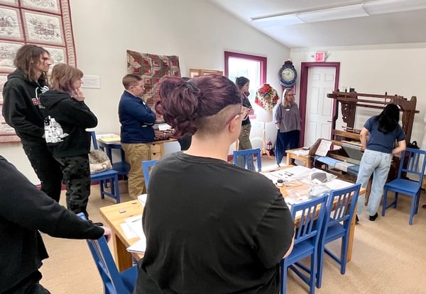 Participants observe a workshop on cleaning decorative arts at Gammelgarden Museum, with a woman demonstrating at a loom