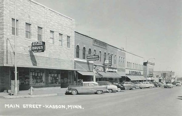 Kasson Street in 50's Drug Store, Hardware Store, Hotel & Cafe, Leutholds. Leutholds and Drug Store have been upgraded. Drug Store sign says Rollins Juhnke & Walter Anderson