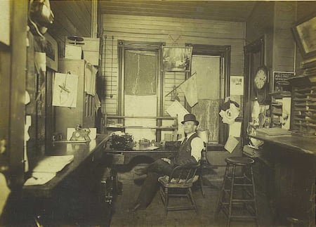 Sepia photograph of Charley Fitzpatrick seated in the cluttered wooden office of the St. Vincent depot station, circa 1922