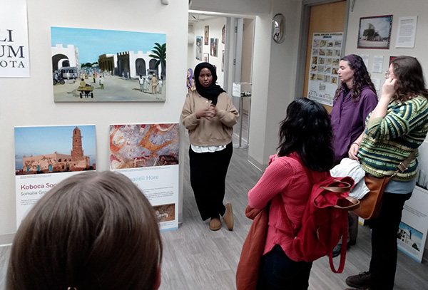 Program Director Maryan Yusuf talking to group of people in front of exhibit artifacts